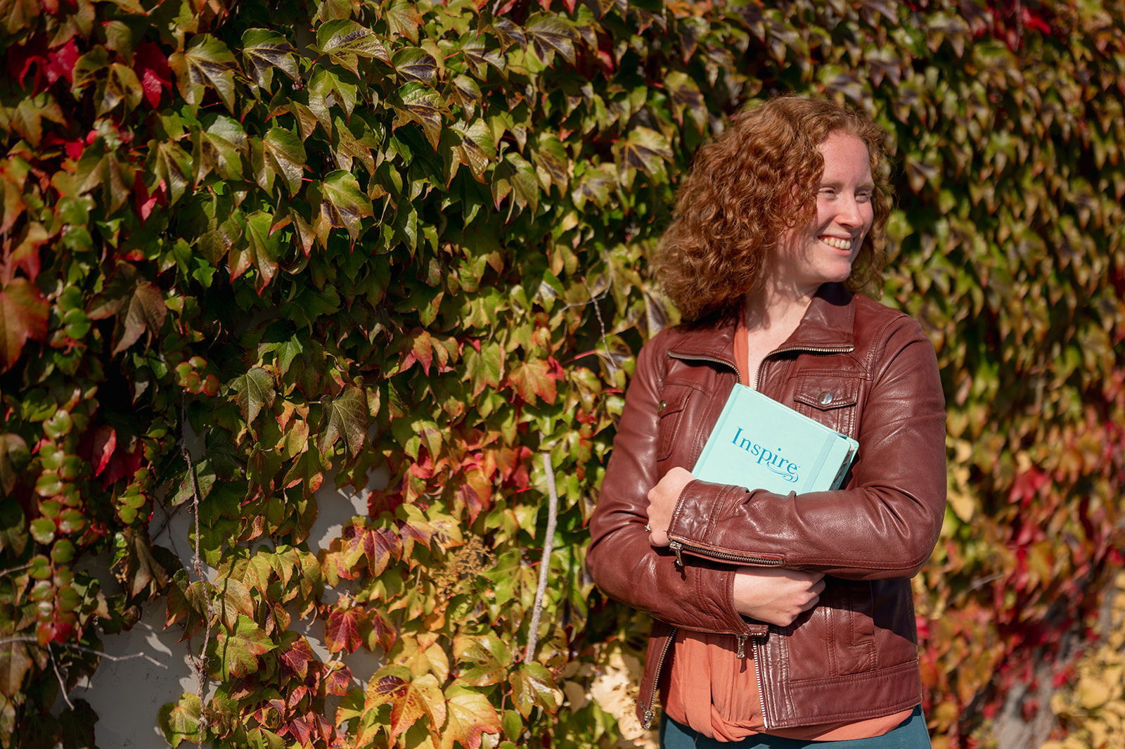 redheaded woman, green hedge, brown jacket, blue journal. www.sarahbeisel.com